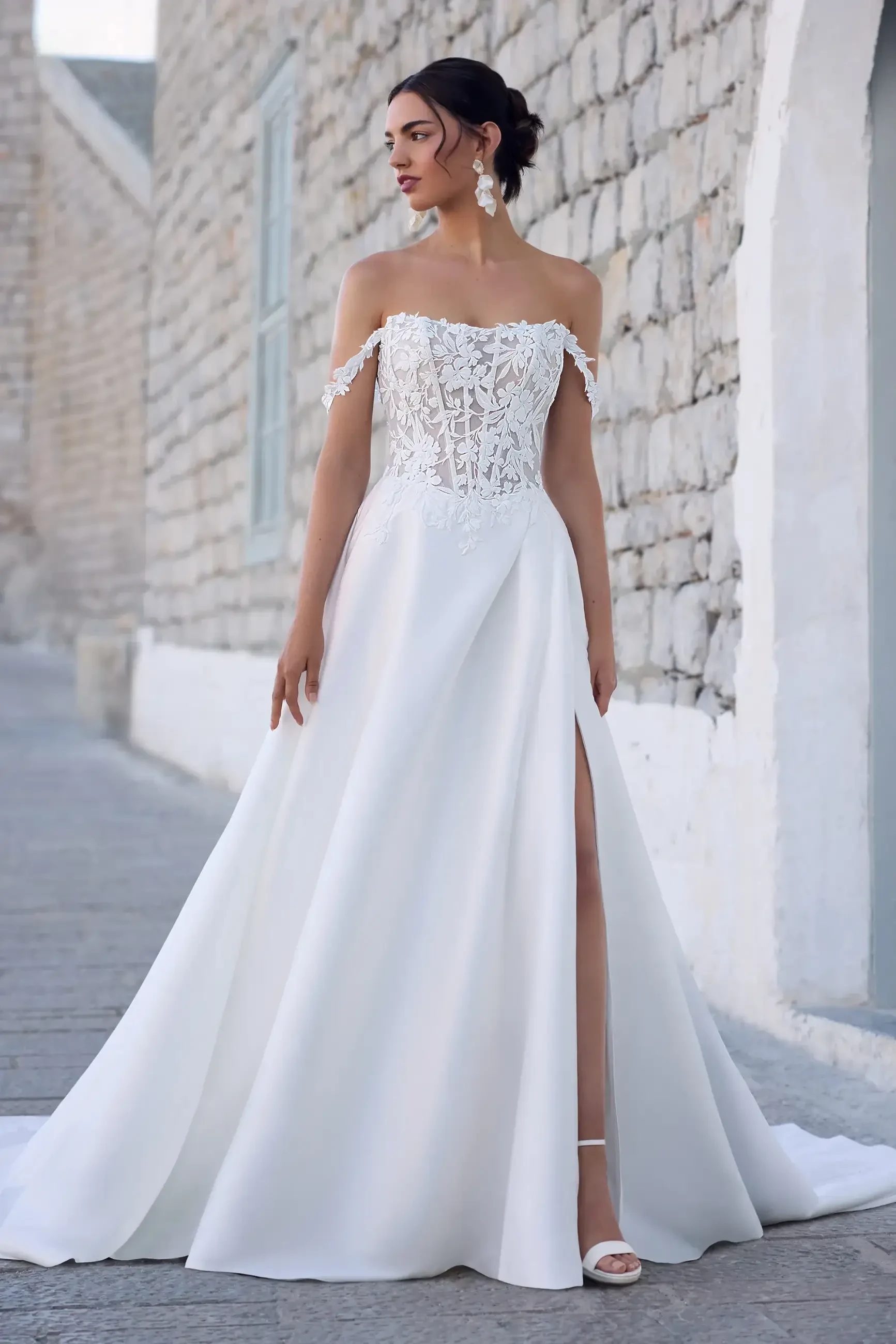 model is wearing an off the shoulder a-line wedding dress with a slit